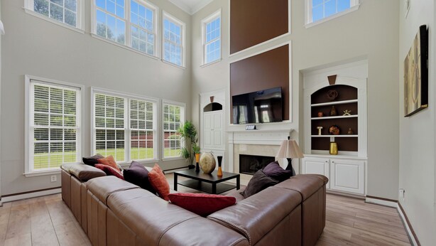 A spacious living room with a brown leather sofa, a fireplace, a flat-screen TV, and a bookshelf. - Modern 4BR Retreat Near ATL Airport & Attractions (Atlanta)