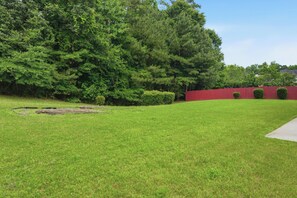 A well-maintained grassy yard with a red fence, trees, and a clear sky. - Modern 4BR Retreat Near ATL Airport & Attractions (Atlanta)