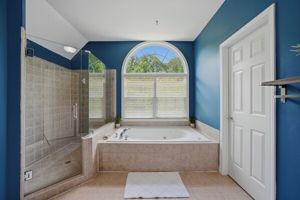 A bathroom with a walk-in shower, a bathtub, and a window with blinds.