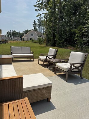 Ein Terrassenbereich im Freien mit Korbmöbeln, darunter eine Couch und Stühle, sowie ein Holztisch.