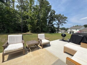 An outdoor patio with two cushioned chairs, a small table, and a grill area. - Old Oaks Oasis: 3-bedroom house in welcoming Oxford (Oxford)