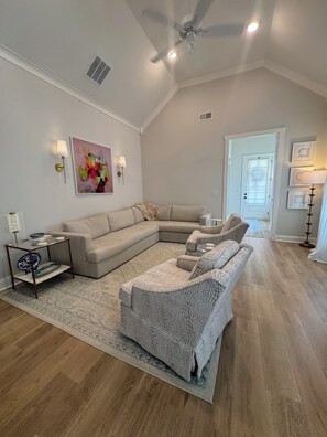 Ein Wohnzimmer mit Ecksofa, Glastisch, gemustertem Teppich und Deckenventilator.