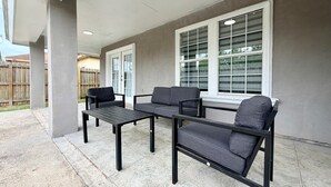 An outdoor patio area with a concrete floor, a black metal table, and two grey sofas. - Casa Pera - Minutes to SpaceX & Port - Spacious! (Brownsville)