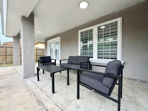 An outdoor patio area with a concrete floor, a black metal table, and two grey sofas. - Casa Pera - Minutes to SpaceX & Port - Spacious! (Brownsville)