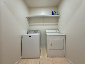 A laundry room with two white washing machines and a shelf above them. - Casa Pera - Minutes to SpaceX & Port - Spacious! (Brownsville)