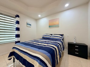 A bedroom with a bed, a nightstand, a window with blinds, and a painting on the wall. - Casa Pera - Minutes to SpaceX & Port - Spacious! (Brownsville)