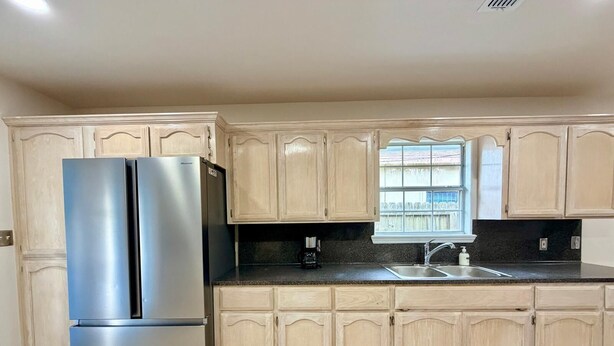 A kitchen with two stainless steel refrigerators, a black countertop, a sink, and light wooden cabinets. - Casa Pera - Minutes to SpaceX & Port - Spacious! (Brownsville)