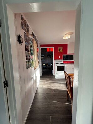 Ein Flur, der zu einer Küche führt, mit weißen Schränken, einer roten Akzentwand und einer Deckenleuchte.