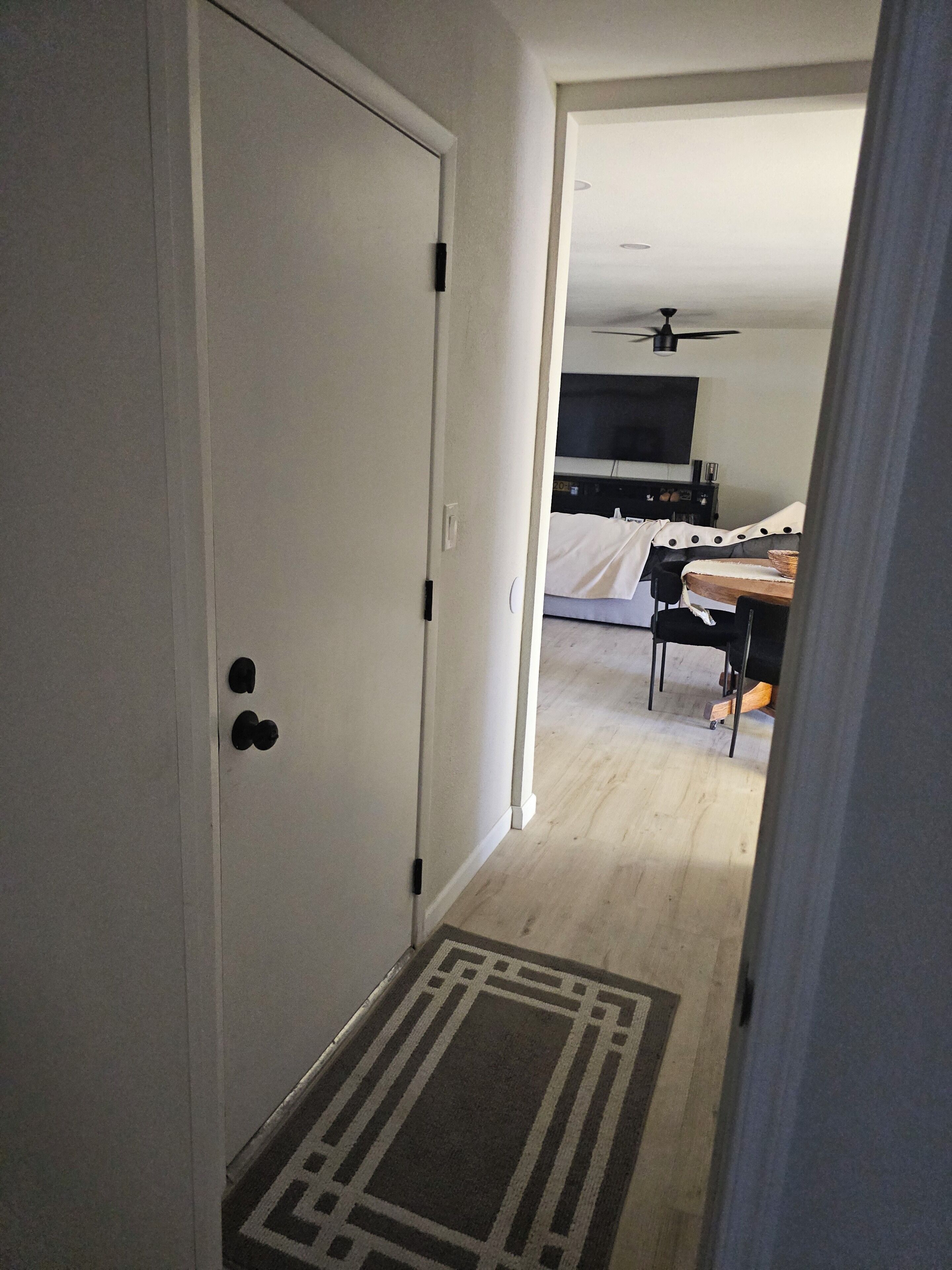 A hallway leading to a bedroom with a bed, a TV, and a ceiling fan.