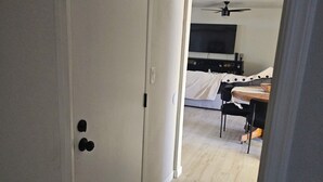Un pasillo que conduce a un dormitorio con una cama, un televisor y un ventilador de techo.