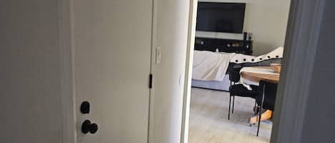 A hallway leading to a bedroom with a bed, a TV, and a ceiling fan.