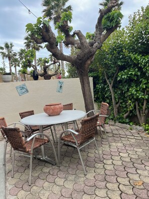 Ein Sitzbereich im Freien mit Korbstühlen und einem runden Tisch, umgeben von einer gepflasterten Terrasse und einem Baum.