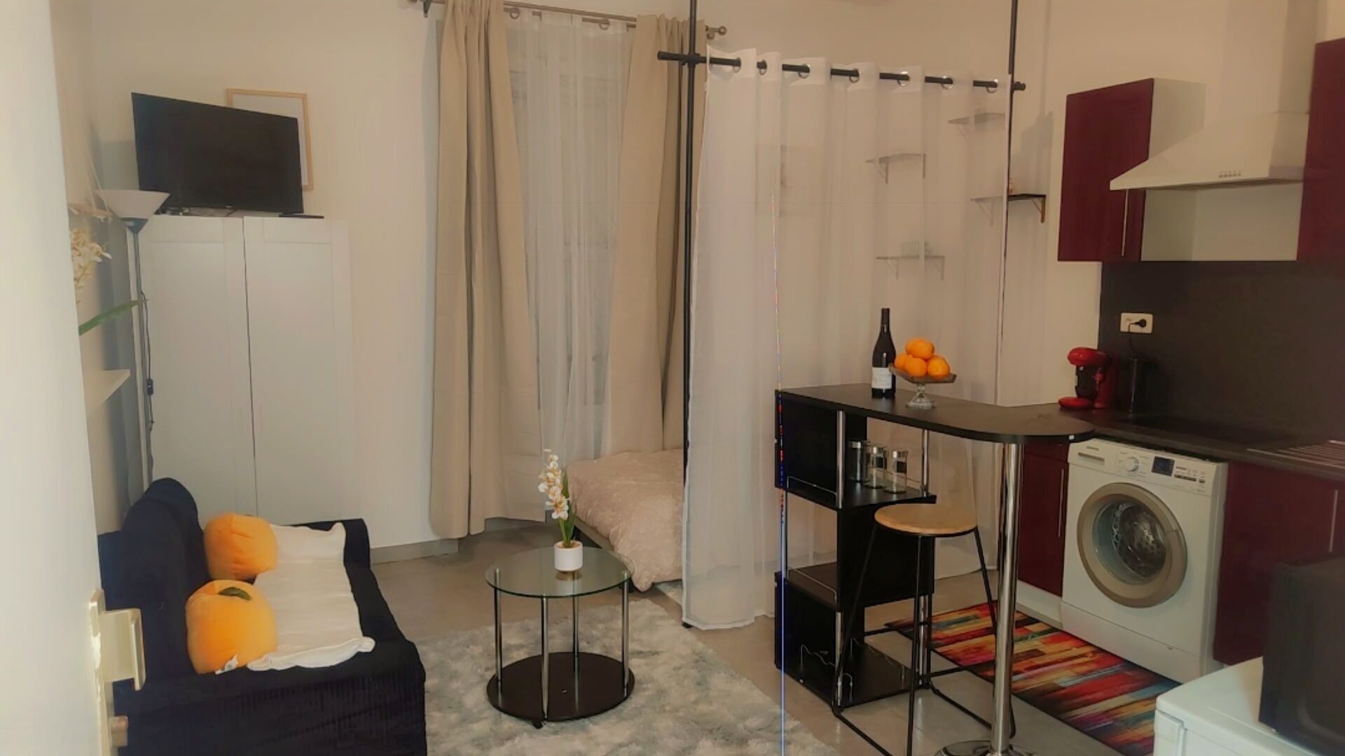 A compact living space with a sofa, a small coffee table, a washing machine, and a television.