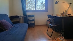Ett rum med en säng, ett skrivbord, en stol och ett fönster med utsikt över träd.