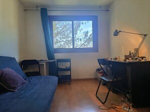 Ein Zimmer mit Bett, Schreibtisch, Stuhl und einem Fenster mit Blick auf Bäume.