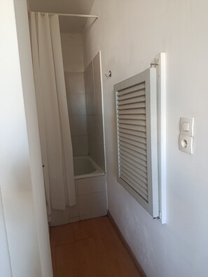 Ein Badezimmer mit Dusche, Toilette und einem Fenster mit Jalousien.