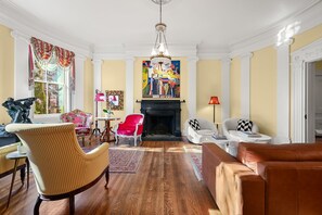 A spacious living room with a fireplace, a chandelier, and a large painting on the wall.