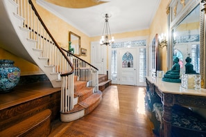 A grand staircase with ornate railings, a chandelier, and a decorative mirror.
