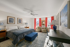 Une chambre à coucher avec un lit, un bureau, une chaise, un ventilateur de plafond et une fenêtre avec des rideaux rouges.