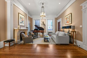 A spacious living room with a grand piano, a fireplace, and a chandelier. - Boston Beacon Hill: The Aldrich House (Boston)