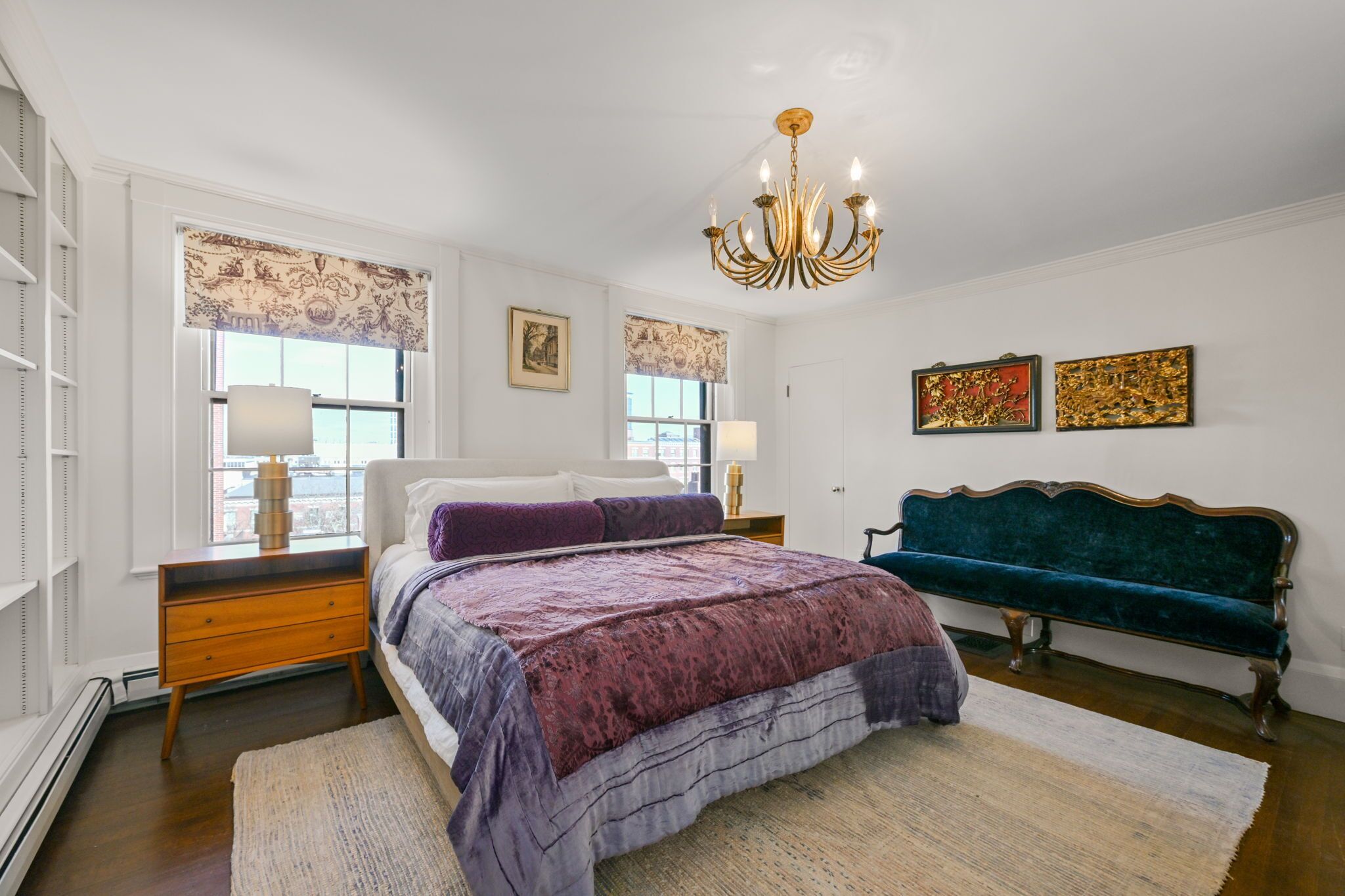 Een slaapkamer met een bed, een bankje, een kroonluchter en kunstwerken aan de muren.