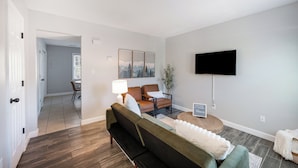 Una sala moderna con un sofá, un televisor y un comedor al fondo.