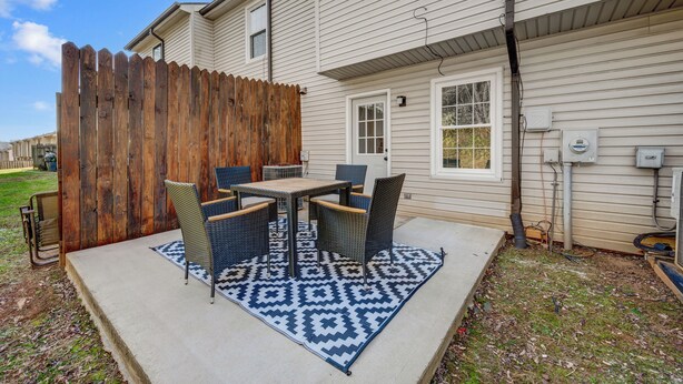 Un patio con mesa y sillas, cerca de madera y una casa con revestimiento y ventanas.