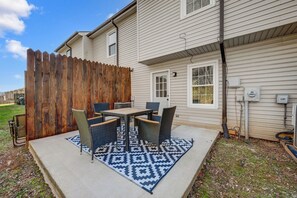 Une terrasse avec une table et des chaises, une clôture en bois et une maison avec un revêtement extérieur et des fenêtres.