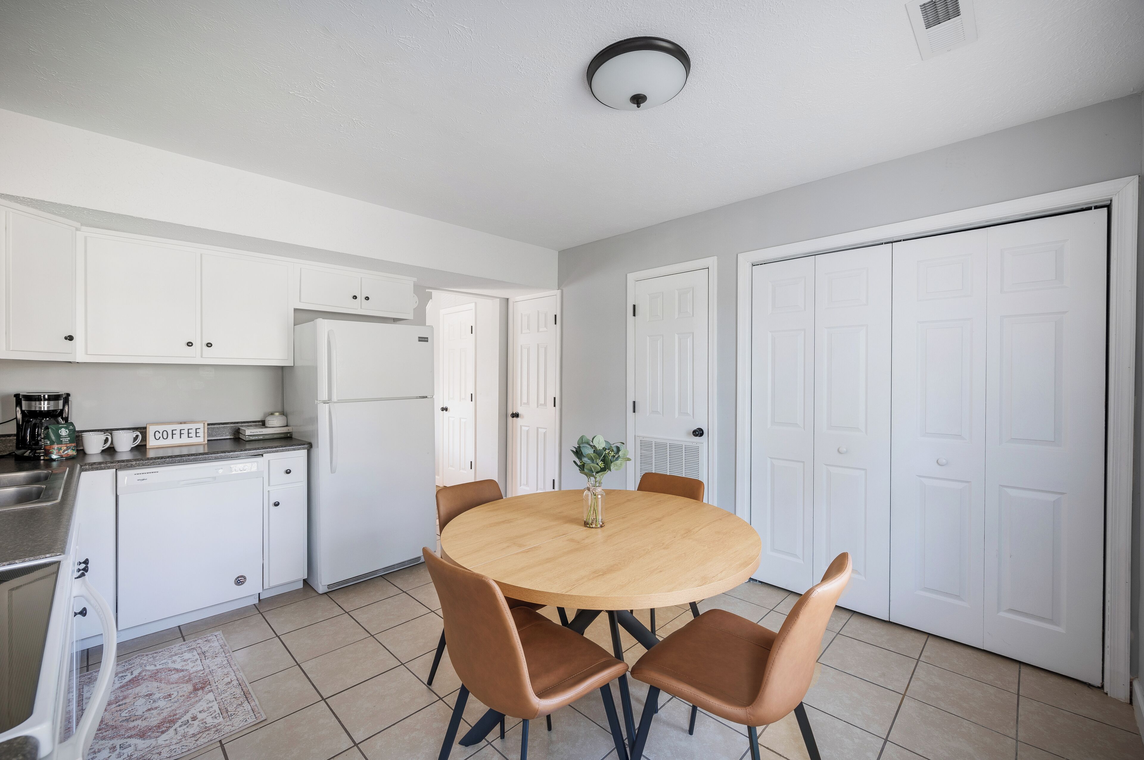 A modern kitchen with white cabinets, a round wooden table, and brown chairs.