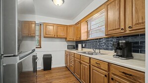 A kitchen with wooden cabinets, a stainless steel refrigerator, a microwave, a coffee maker, and a trash can.