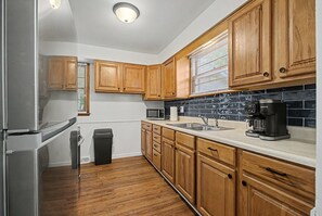 A kitchen with wooden cabinets, a stainless steel refrigerator, a microwave, a coffee maker, and a trash can.