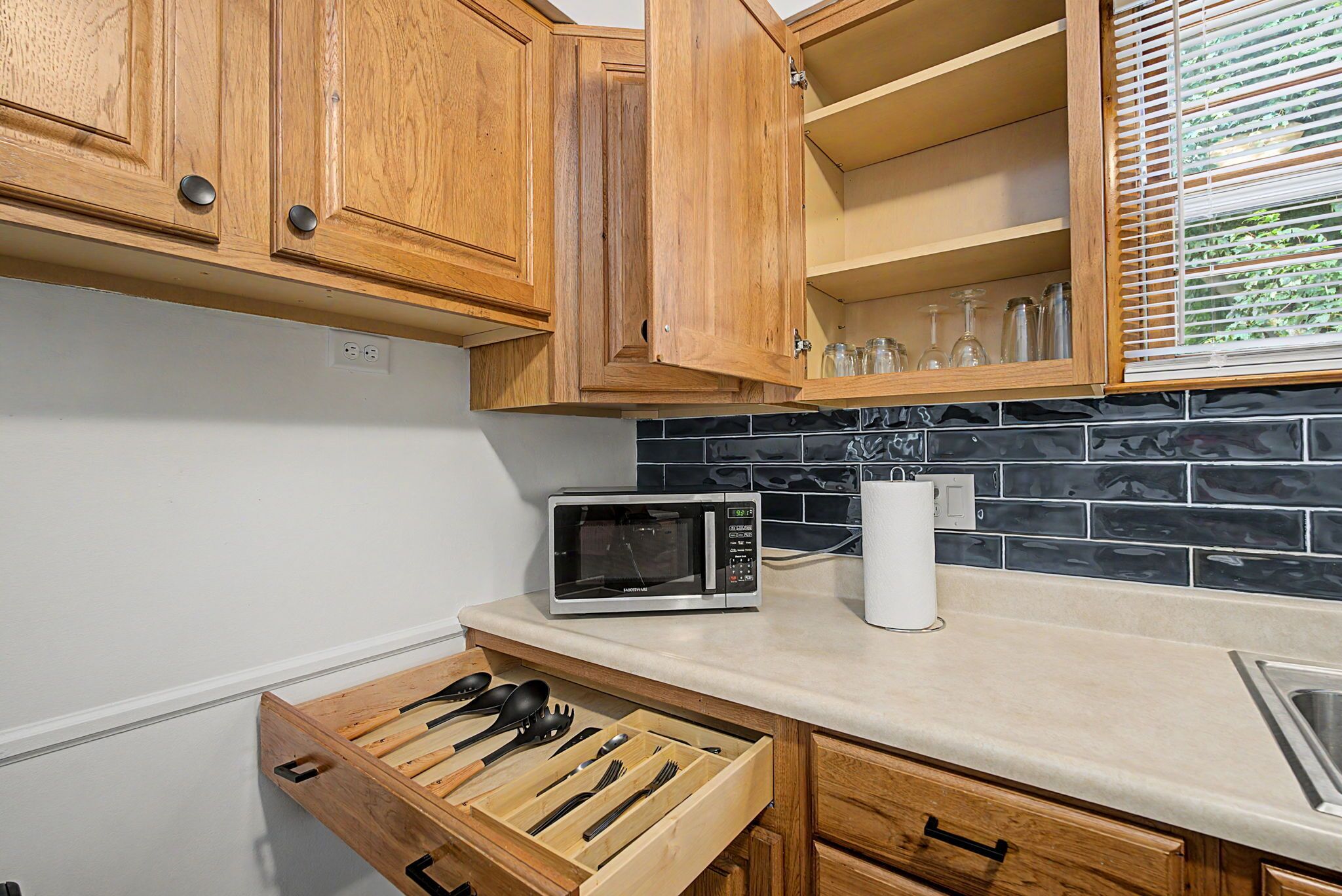 A kitchen with wooden cabinets, a microwave, a paper towel holder, and a utensil drawer.