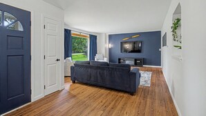 A modern living room with a dark sofa, a flat-screen TV, and a wooden floor.