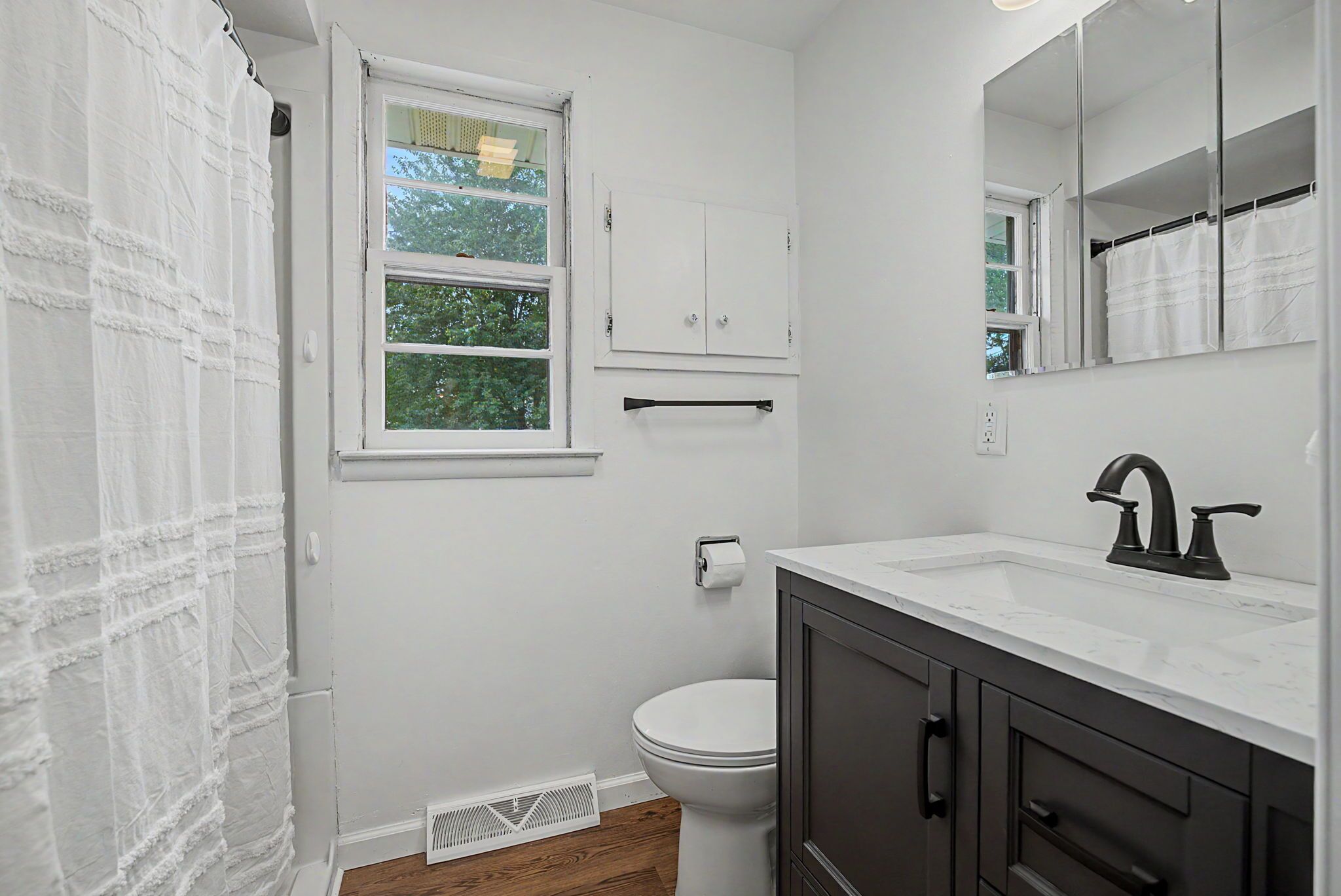 A bathroom with a toilet, sink, mirror, and window.