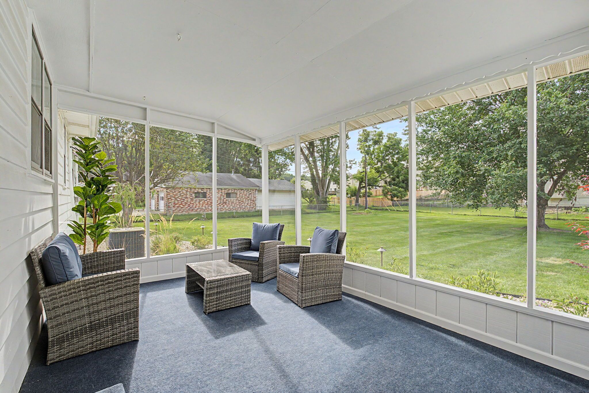 Un patio cubierto con mobiliario de mimbre y vista a un jardín.