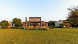 Una moderna casa a due piani con un ampio prato anteriore, un camino ben visibile e un piccolo spazio relax all'aperto.