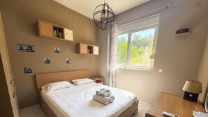 Ett hotellrum med en stor säng, sängbord, ett skrivbord med en lampa och ett fönster med utsikt över grönområden.