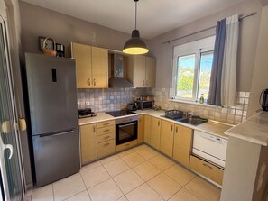 A modern kitchen with stainless steel appliances, wooden cabinets, and a window with curtains. - Villa Fountain (Pool, Garden, BBQ, Starlink, Wood House) (Afantou)