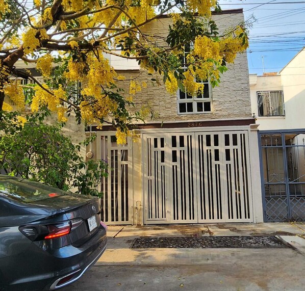 A residential building with a gated entrance, a parked car, and a tree with yellow flowers.