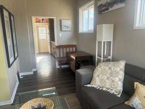 A living room with a sofa, a dining table, and a kitchen in the background. - Cara’s Oasis (Trail)