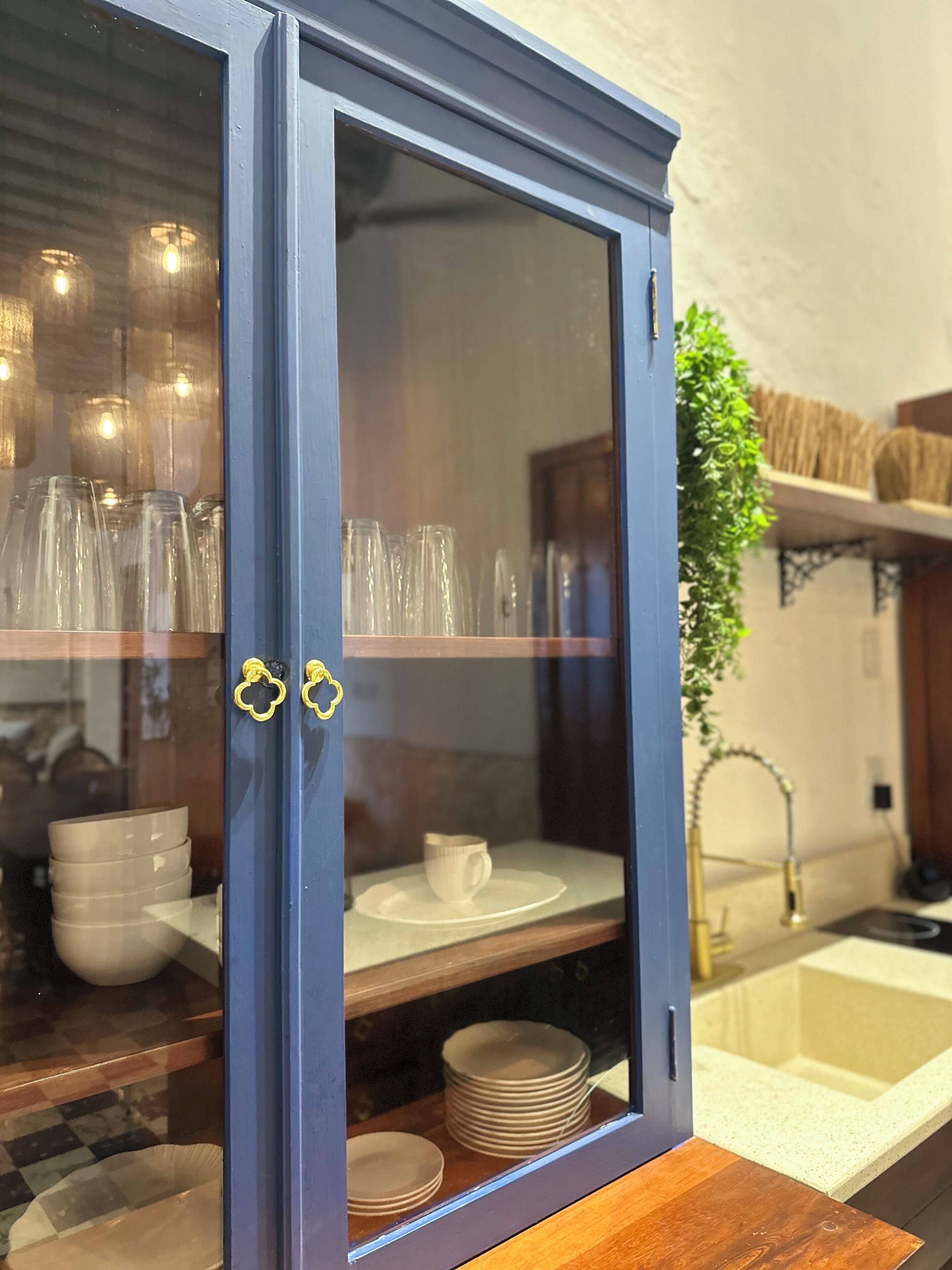 A blue cabinet with glass doors containing stacked plates and a white cup.