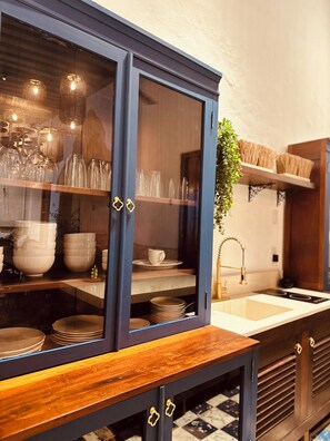 Eine Küche mit einem dunkelblauen Schrank, der Glaswaren und Geschirr enthält, einer Holz Arbeitsplatte und einer hängenden Pflanze.