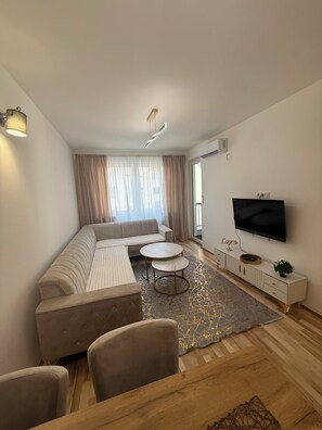 A modern living room with a sofa, two side tables, a TV, and a patterned rug. - Daky home near AirPort,tram and City center (Sarajevo)