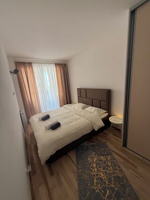 A hotel room with a bed, a bedside table, a window with curtains, and a door. - Daky home near AirPort,tram and City center (Sarajevo)