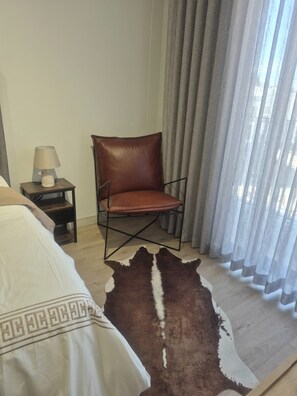 Ein Hotelzimmer mit einem Bett, einem Ledersessel, einem kleinen Tisch mit Lampe und einem großen Fenster mit Vorhängen.
