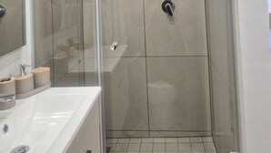 Ein modernes Badezimmer mit einer gläsernen Duschkabine, einem weißen Waschbecken und einem Spiegel.