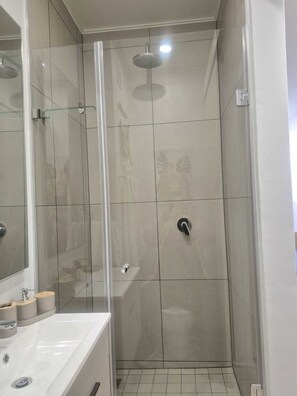 A modern bathroom with a glass-enclosed shower, a white sink, and a mirror. - Charming Studio in beautiful Johannesburg, perfect for your stay. (Johannesburg)