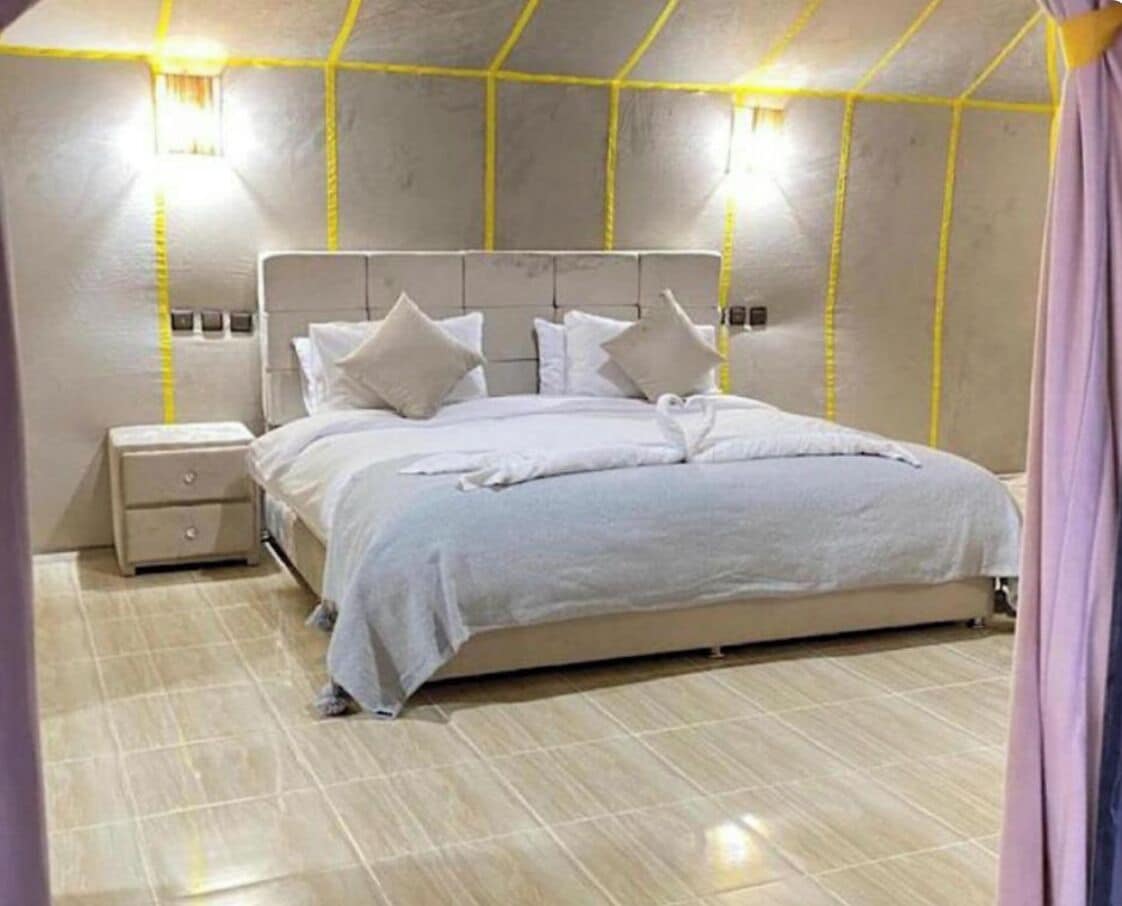 Un dormitorio con cama, mesita de noche e iluminación en la pared.