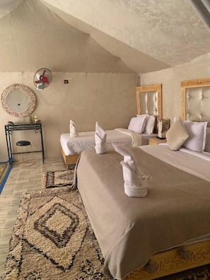 Habitación de hotel con dos camas, un espejo redondo, una mesita con un taburete y una alfombra estampada.