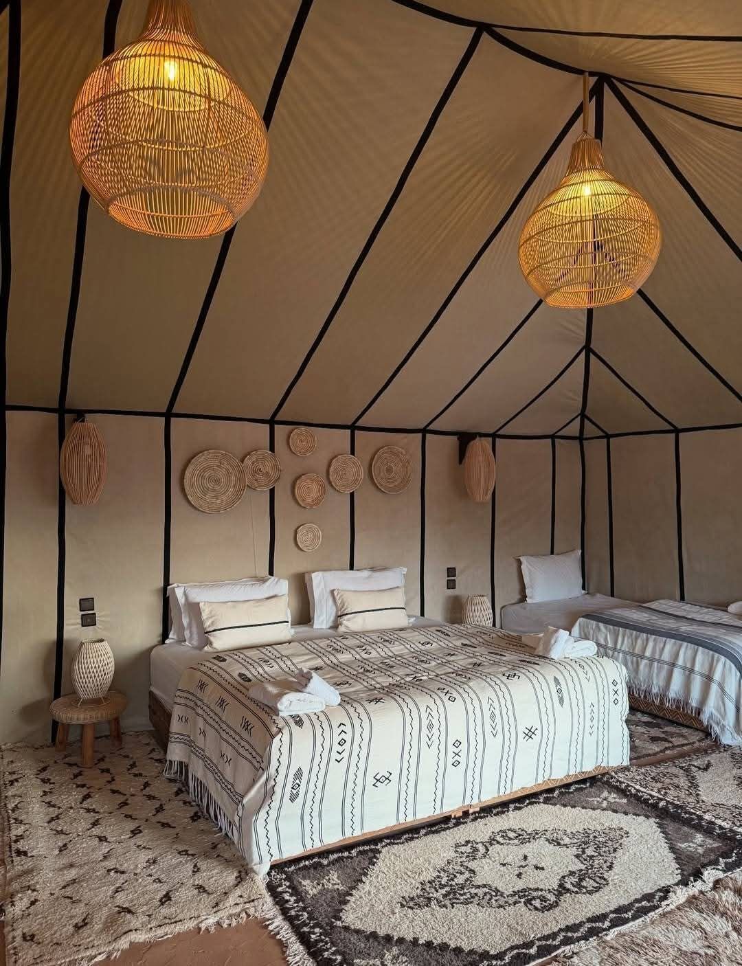 Et teltformet rum med to senge, vævede lamper og mønstrede tæpper.
